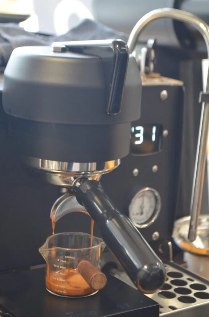 Espresso extracting into a glass, with the pressure gauge and shot timer visible